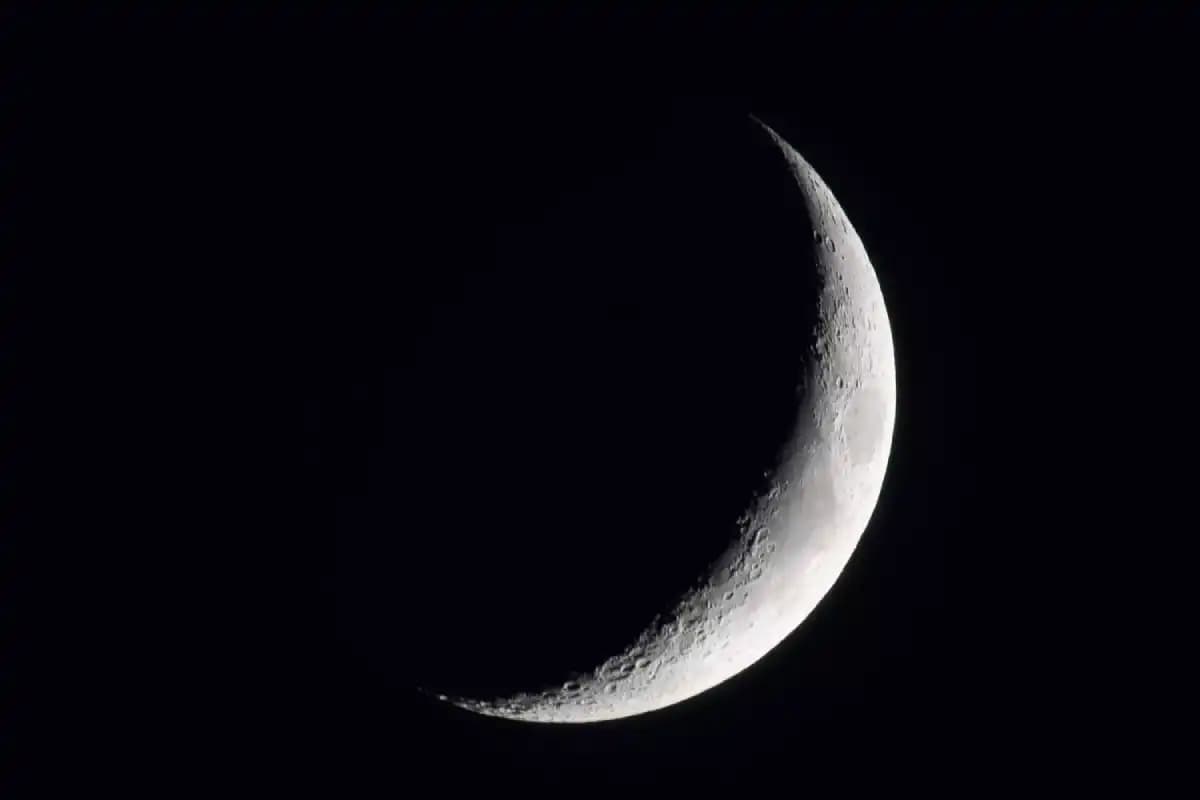 New moon in a clear night sky, showcasing a dark silhouette against the stars.