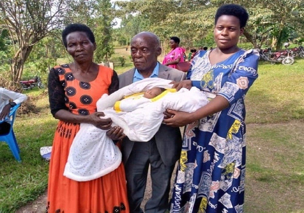 Homme de 83 ans tenant son bébé, sourire aux lèvres, moment émouvant de paternité tardive.