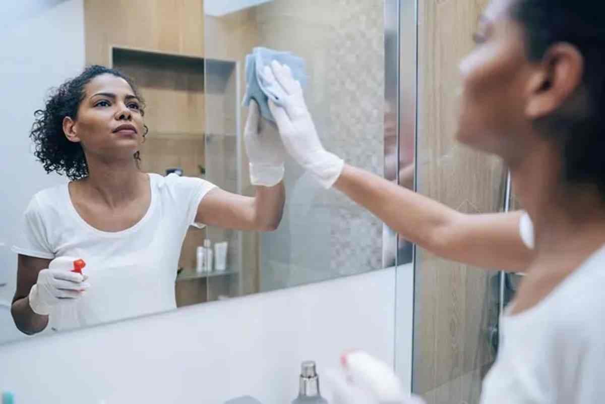 une femme en train de nettoyer un miroir de salle de bain