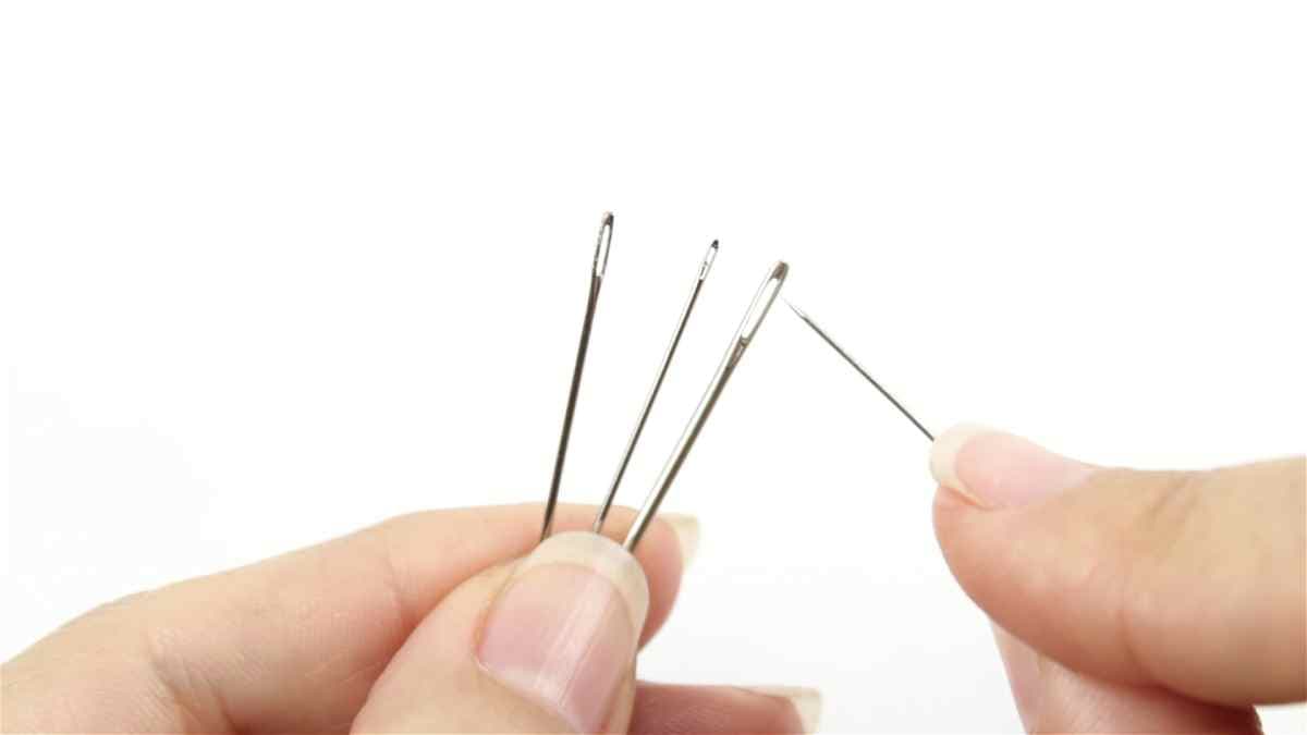 deux mains gardant trois aiguilles et un fil, tentant de l'enfiler