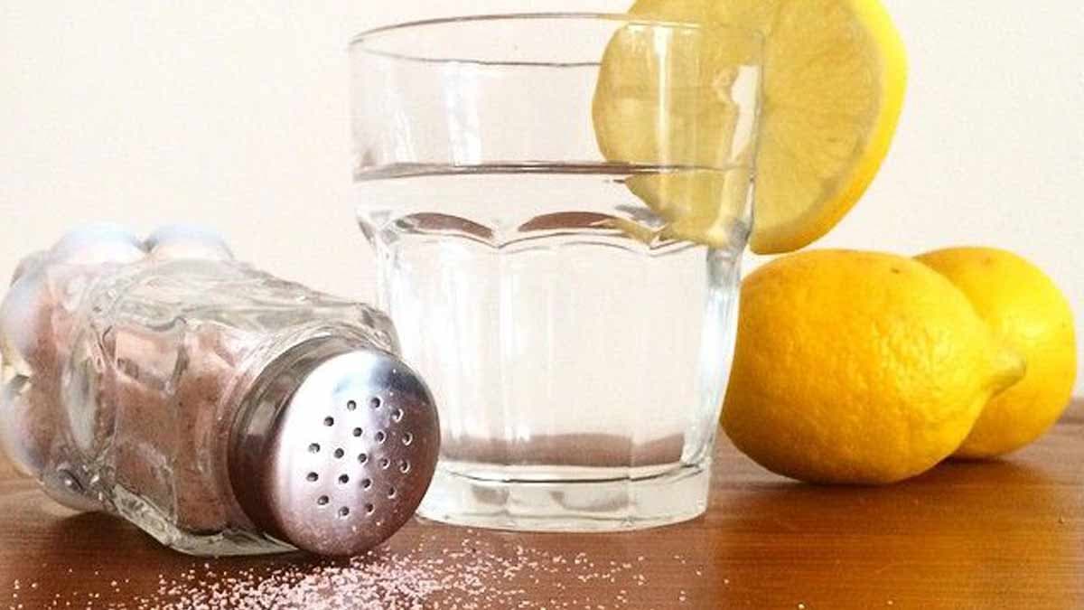 un pot de sel , une tranche de citron et des citron non découpés avec un verre d'eau sur une table