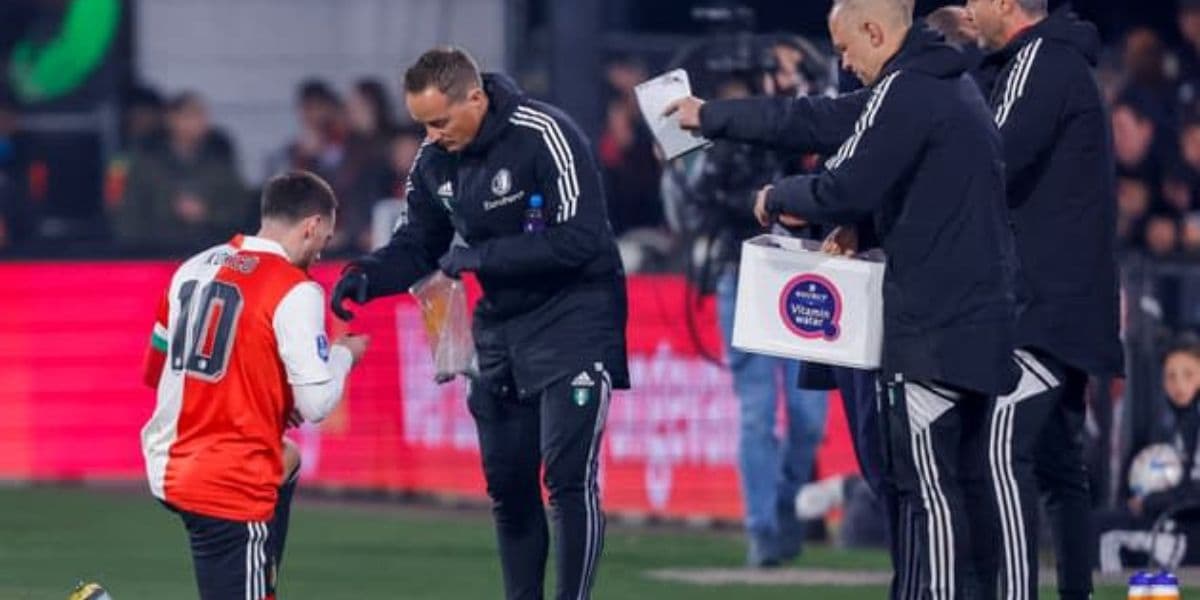 Joueur de football en pause pendant le Ramadan, discutant avec des coéquipiers sur le terrain.