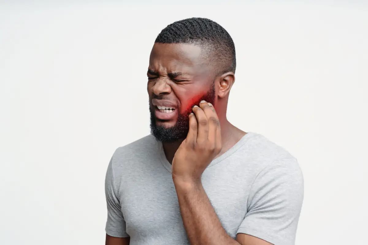 Homme se tenant la joue, visiblement souffrant d'un mal de dent.